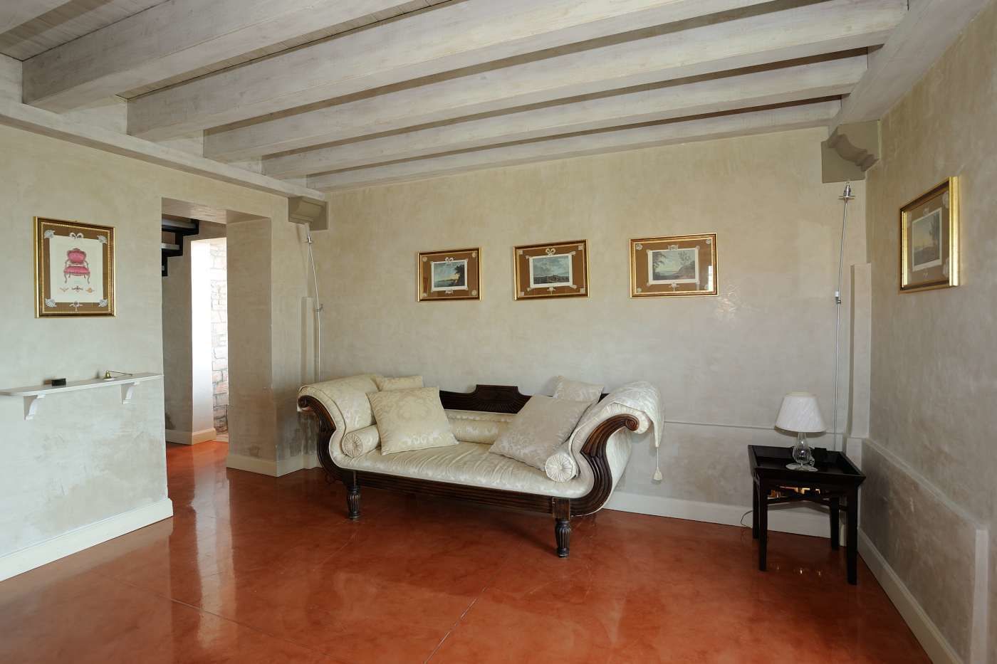 Un salon spacieux avec un canapé de couleur crème, une petite table avec une lampe et des tableaux encadrés accrochés au mur.
