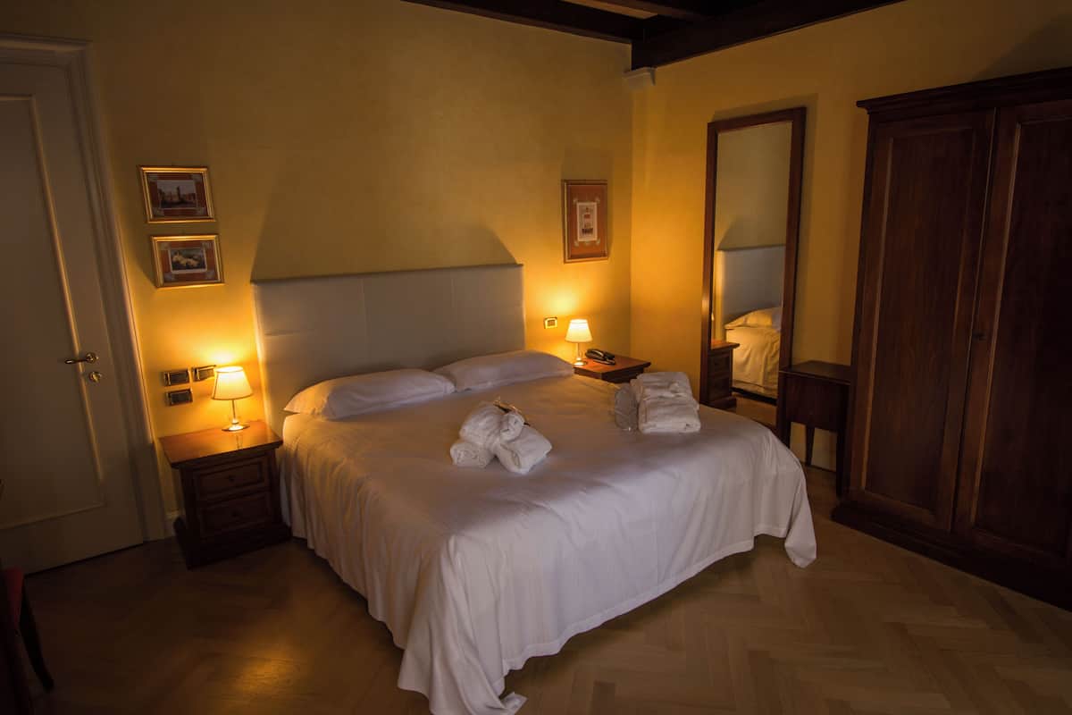 A neatly made bed with white linens and towels, a wooden wardrobe, and two bedside lamps on nightstands.