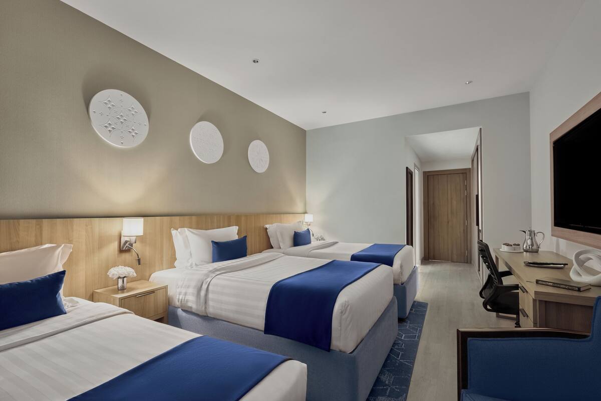 Een hotelkamer met drie bedden, een bureau, een stoel en een televisie.