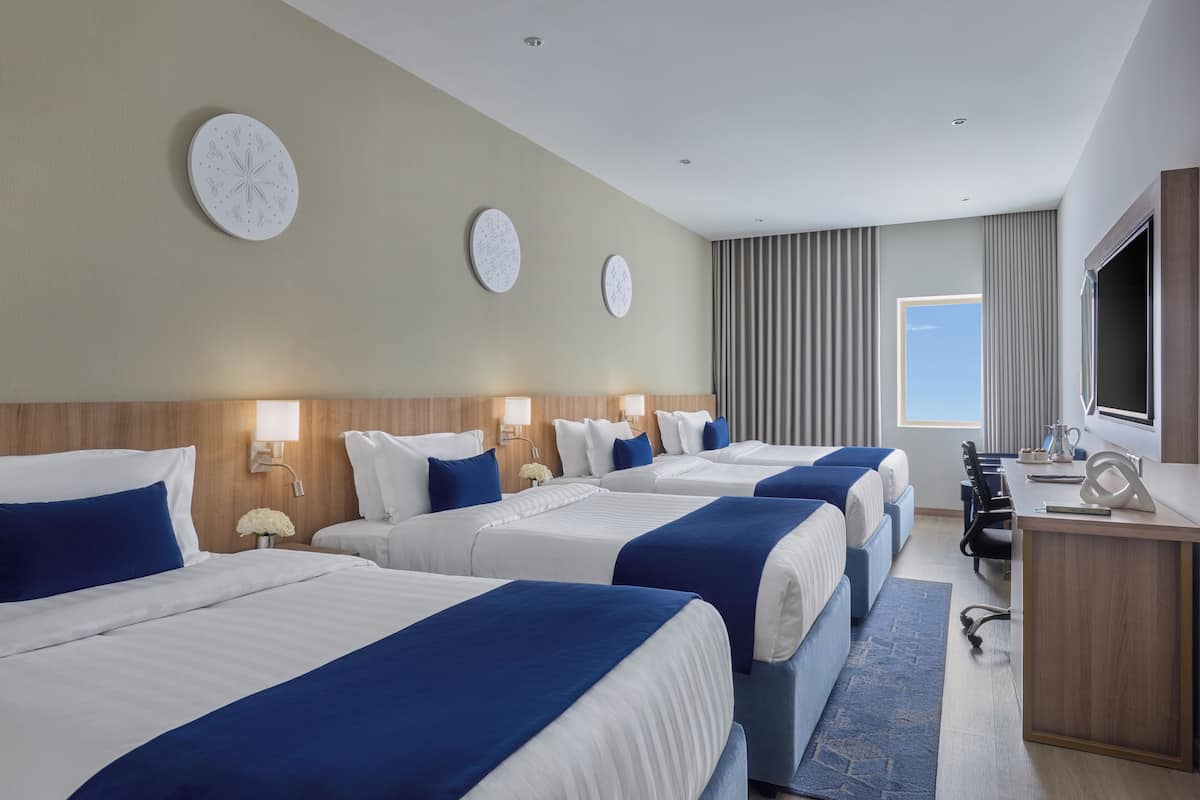 Een hotelkamer met vier bedden, een bureau, een televisie en een raam met gordijnen.