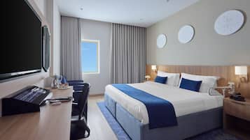 A hotel room with a bed, desk, chair, and a large window.