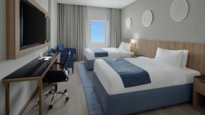 A hotel room with two beds, a desk with a chair, a TV, and a window with curtains.