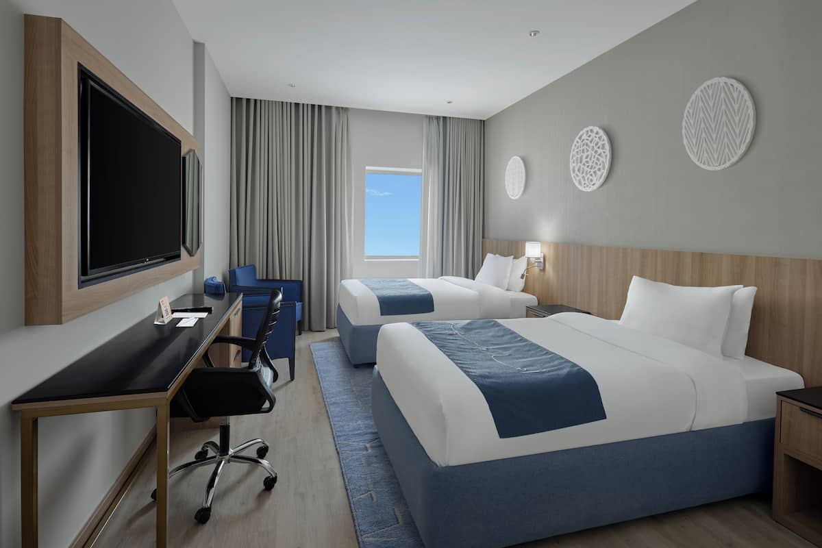 Een hotelkamer met twee bedden, een bureau met stoel, een televisie en een raam met gordijnen.