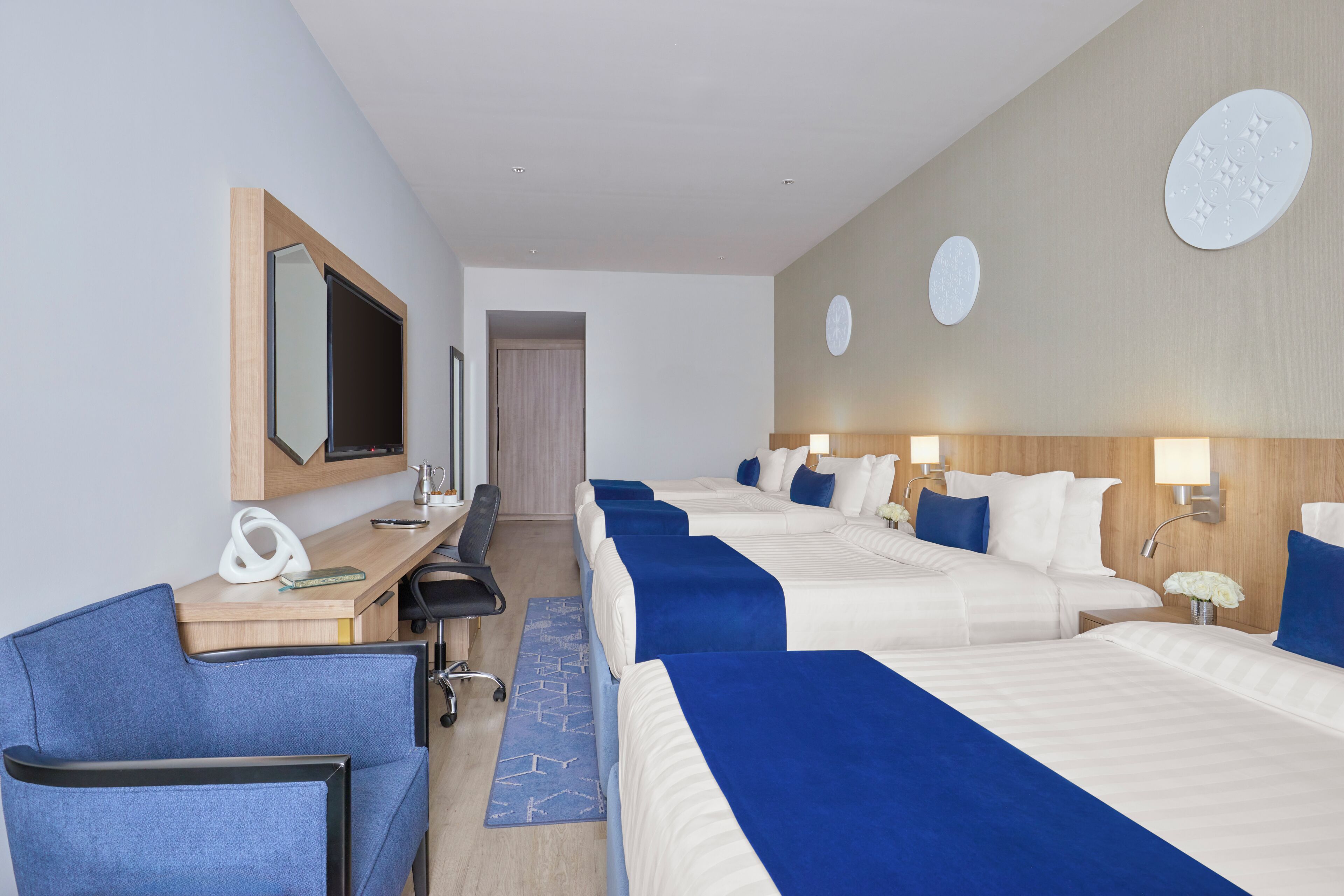 Une chambre d’hôtel avec quatre lits, un bureau, une chaise, une télévision et un miroir.