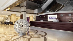 A hotel reception area with a modern design, including a reception desk, a large decorative sphere, and an escalator.