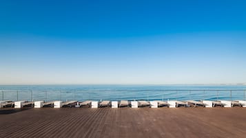 A wooden deck with sun loungers facing a calm sea under a clear sky.