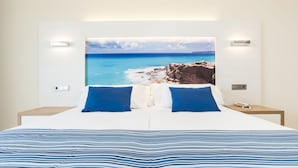 A double bed with a striped blue and white bedspread, two blue pillows, and a large framed picture of a coastal landscape on the wall behind. - Globales Playa Estepona (Estepona)
