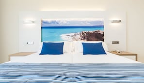 A double bed with a striped blue and white bedspread, two blue pillows, and a large framed picture of a coastal landscape on the wall behind. - Globales Playa Estepona (Estepona)
