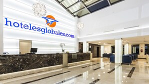 A hotel reception area with a marble counter, a chandelier, and a large logo on the wall. - Globales Playa Estepona (Estepona)