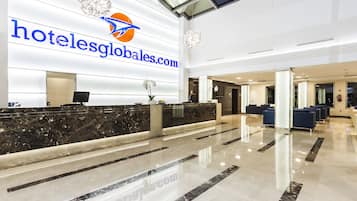 Uma área de recepção de hotel com balcão de mármore, um candelabro e um grande logotipo na parede.