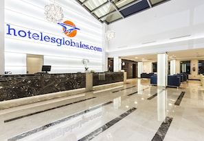 A hotel reception area with a marble counter, a chandelier, and a large logo on the wall. - Globales Playa Estepona (Estepona)