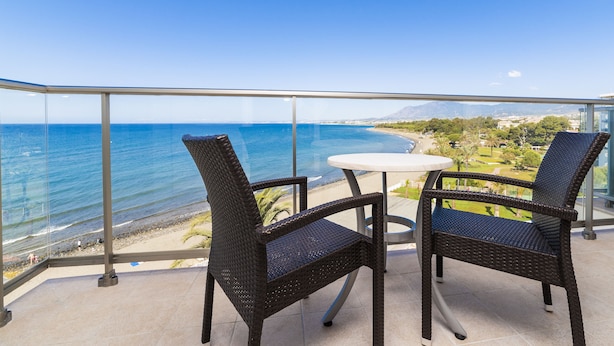 A balcony with two wicker chairs and a small table, overlooking a beach and ocean. - Globales Playa Estepona (Estepona)