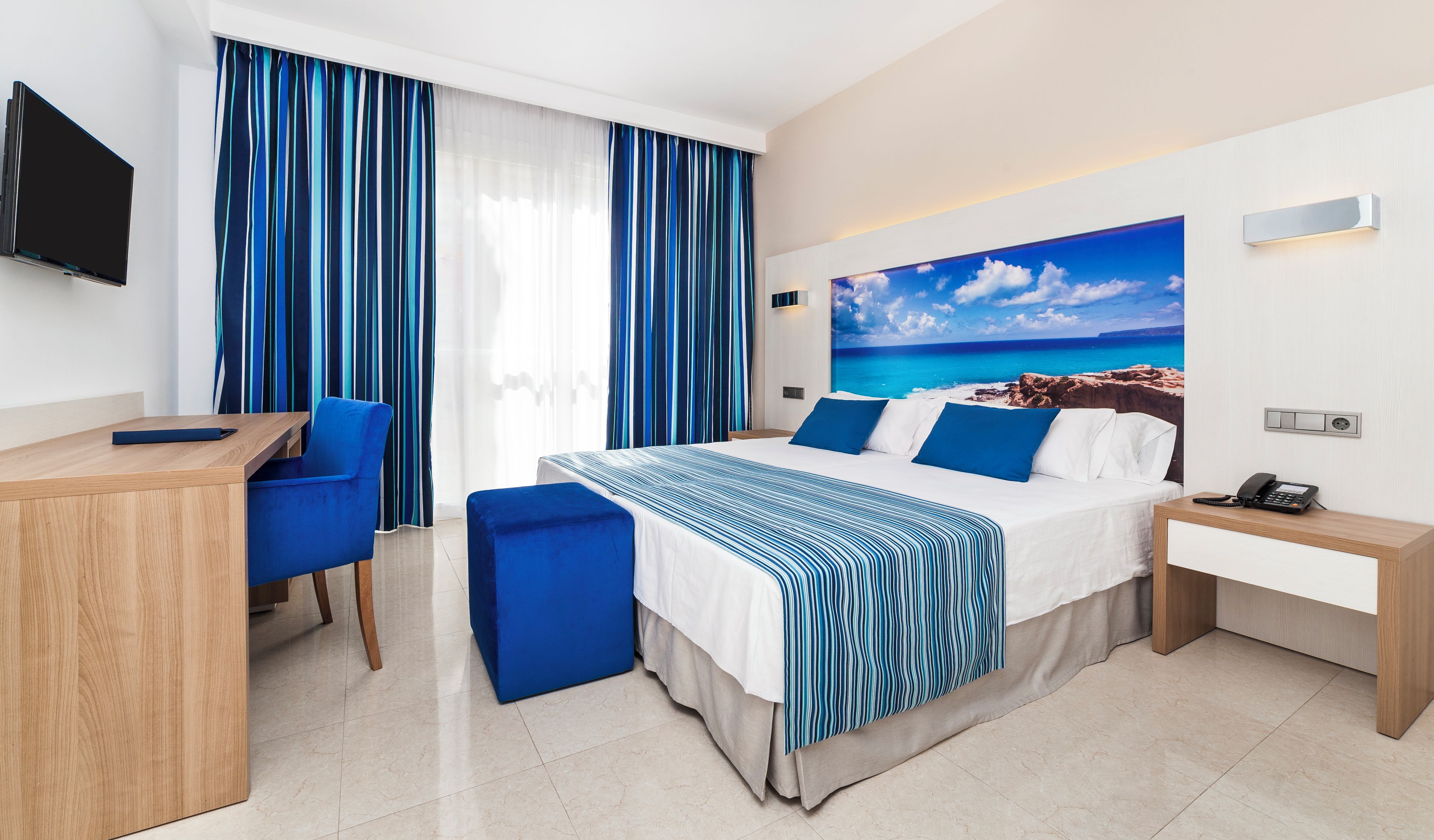 Une chambre d’hôtel équipée d’un lit, d’un bureau, d’une chaise, d’un téléphone et d’une télévision.