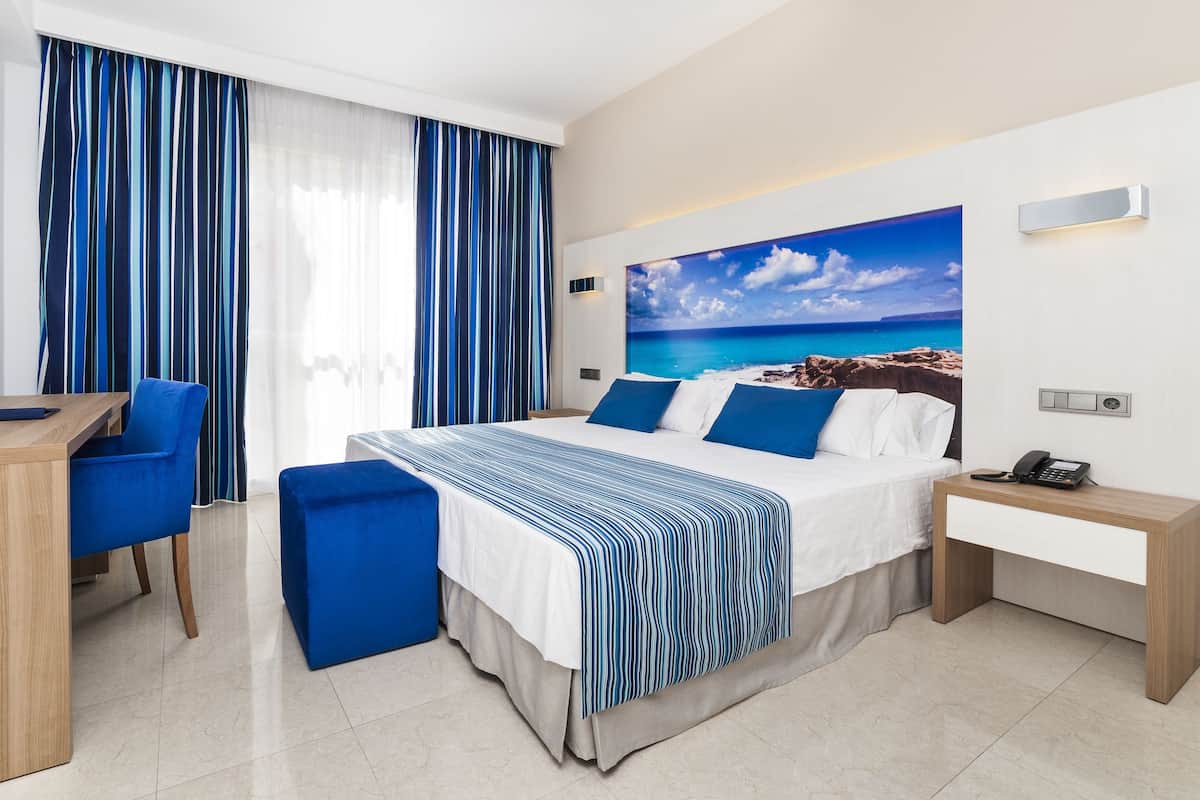 A hotel room with a bed, a desk, a chair, a phone, and a TV.