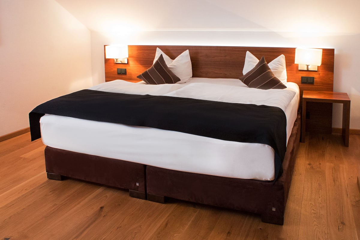 A neatly made bed with a wooden headboard, two bedside tables with lamps, and a wooden floor.