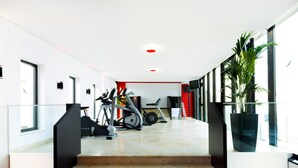 Un espacio interior moderno con una escalera que sube a un nivel superior, equipo de ejercicio y una planta grande en maceta.