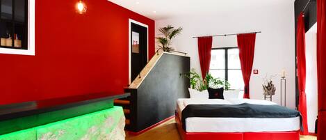 Un dormitorio moderno con una pared de acento roja, una cama con cabecera blanco y negro, una escalera y un banco iluminado con luz verde.