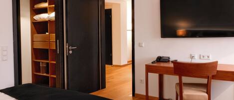 Una habitación de hotel con cama, un escritorio con silla, televisor montado en la pared y un armario con espejo.