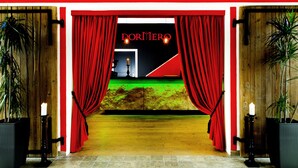 Entrada de teatro con cortinas rojas, un escenario con piso verde y un letrero que dice "DORNER".