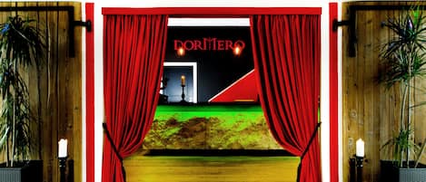 Entrada de teatro con cortinas rojas, un escenario con piso verde y un letrero que dice "DORNER".