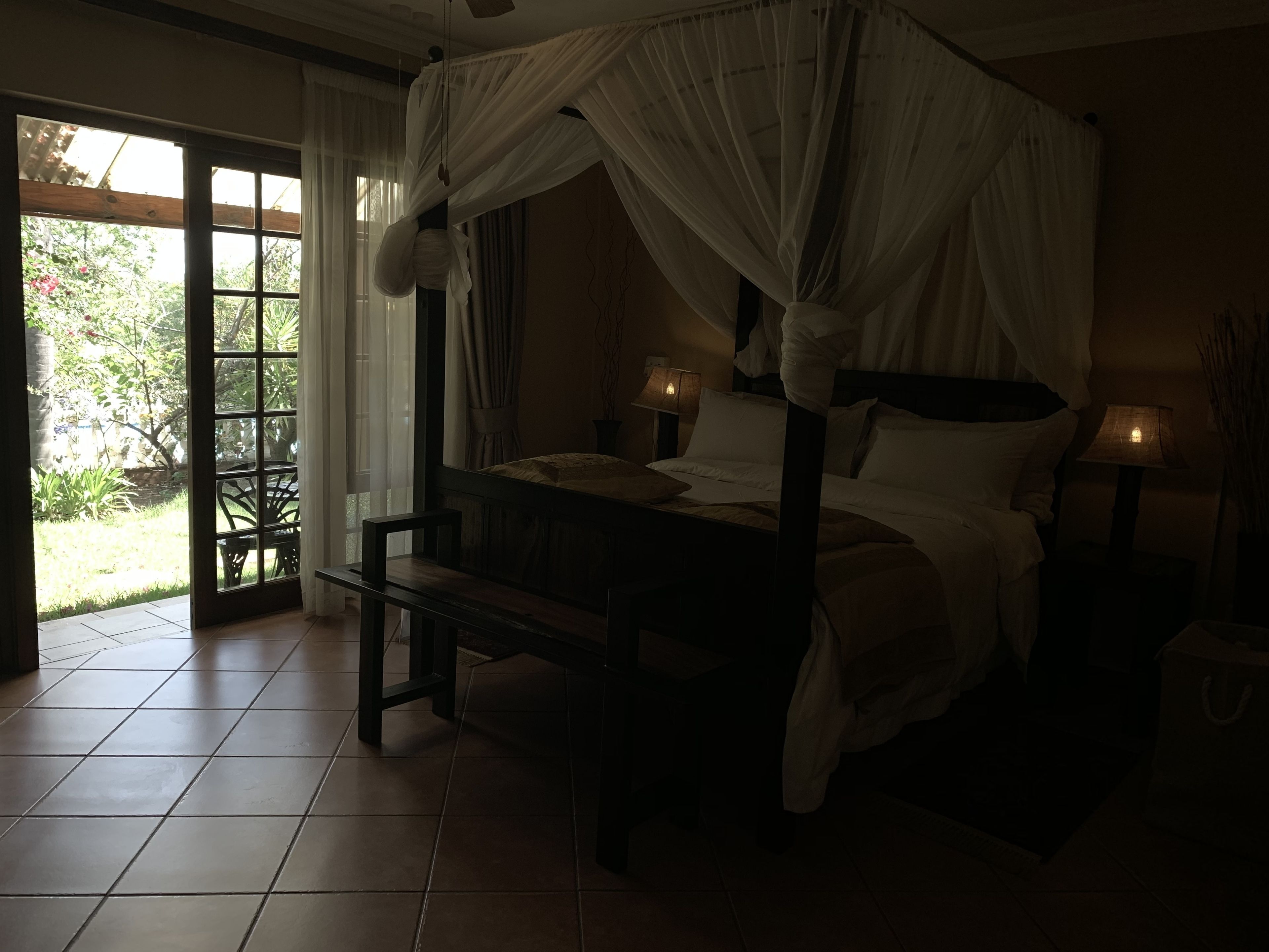 A dimly lit bedroom with a four-poster bed, a bench, and two bedside lamps.
