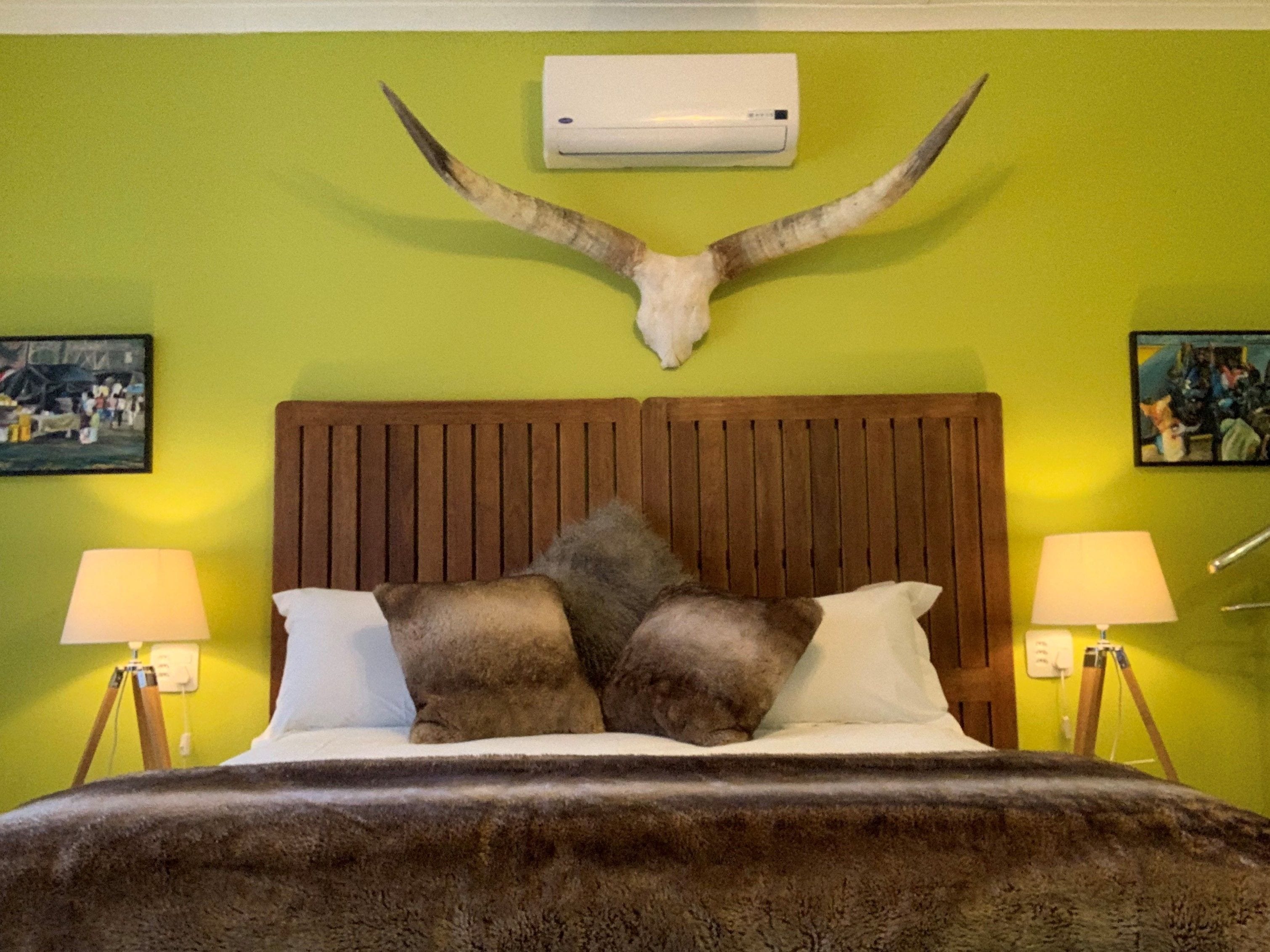 A room with a bed, two lamps, a wooden headboard, and a mounted animal skull on the wall.