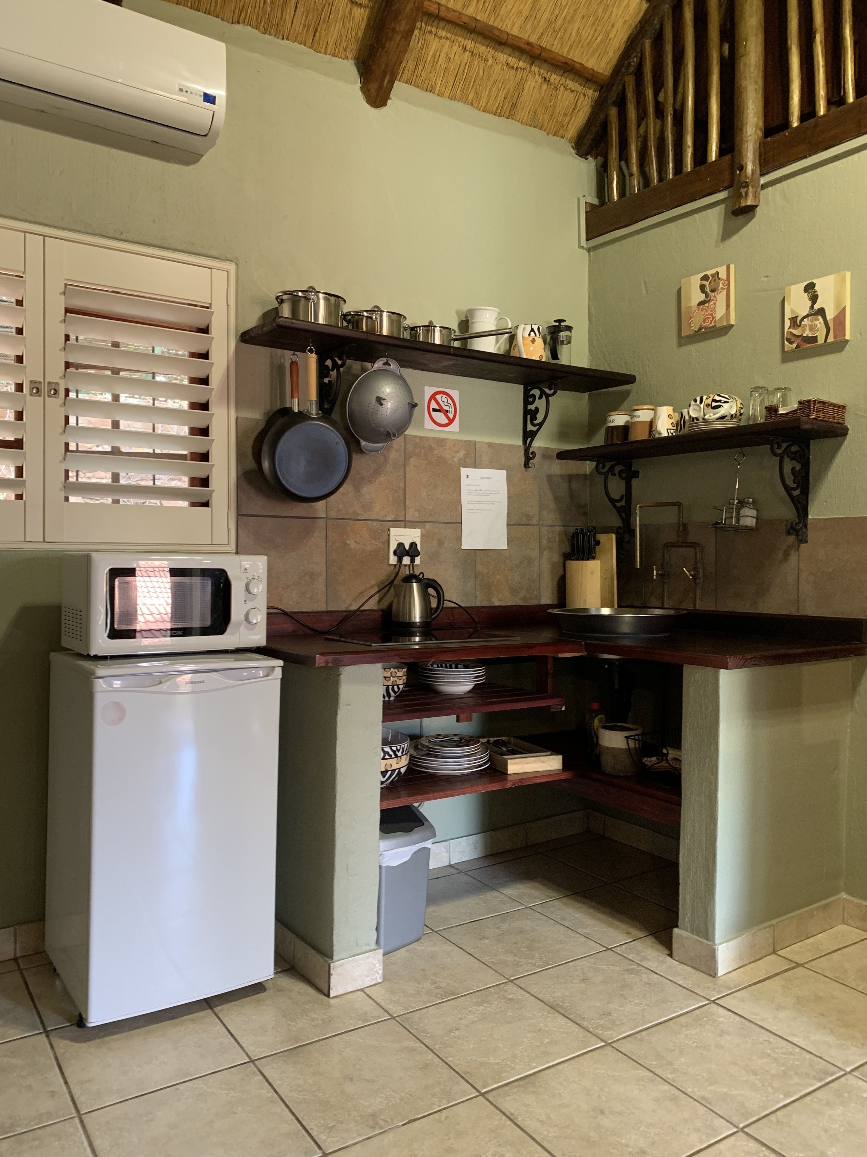 A compact kitchen with a microwave, a small refrigerator, and a shelf with kitchen utensils and cookware.