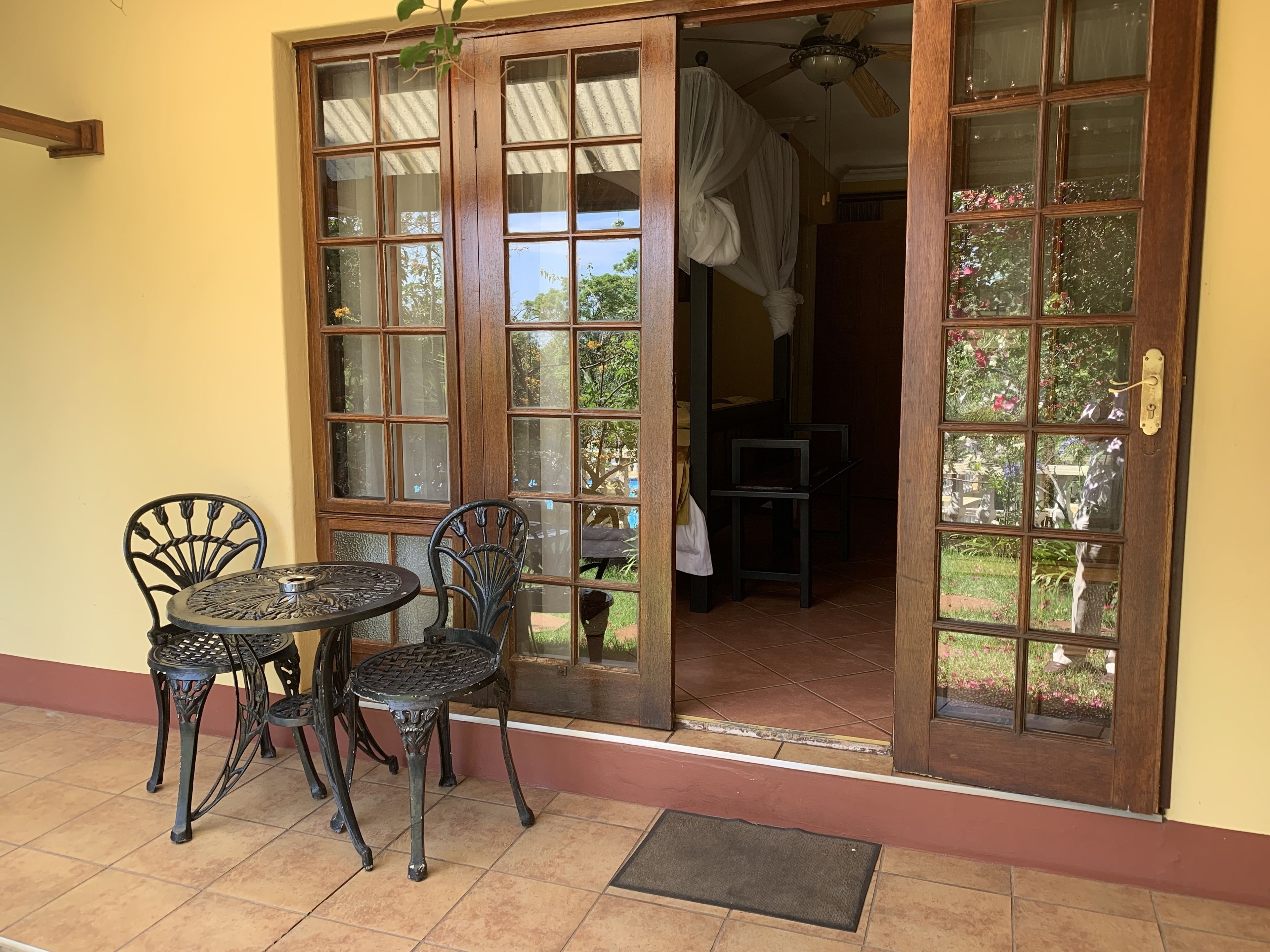 Un patio con una mesa y sillas, una puerta de madera con paneles de vidrio y vistas al jardín.