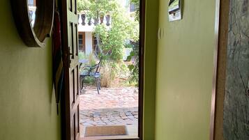Un pasillo con pared verde, una puerta de madera que da a un patio con suelo de baldosas y un cuadro enmarcado a la derecha.