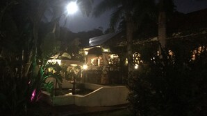 Une vue nocturne d’un bâtiment dont les fenêtres sont illuminées et dont le jardin est bien éclairé.
