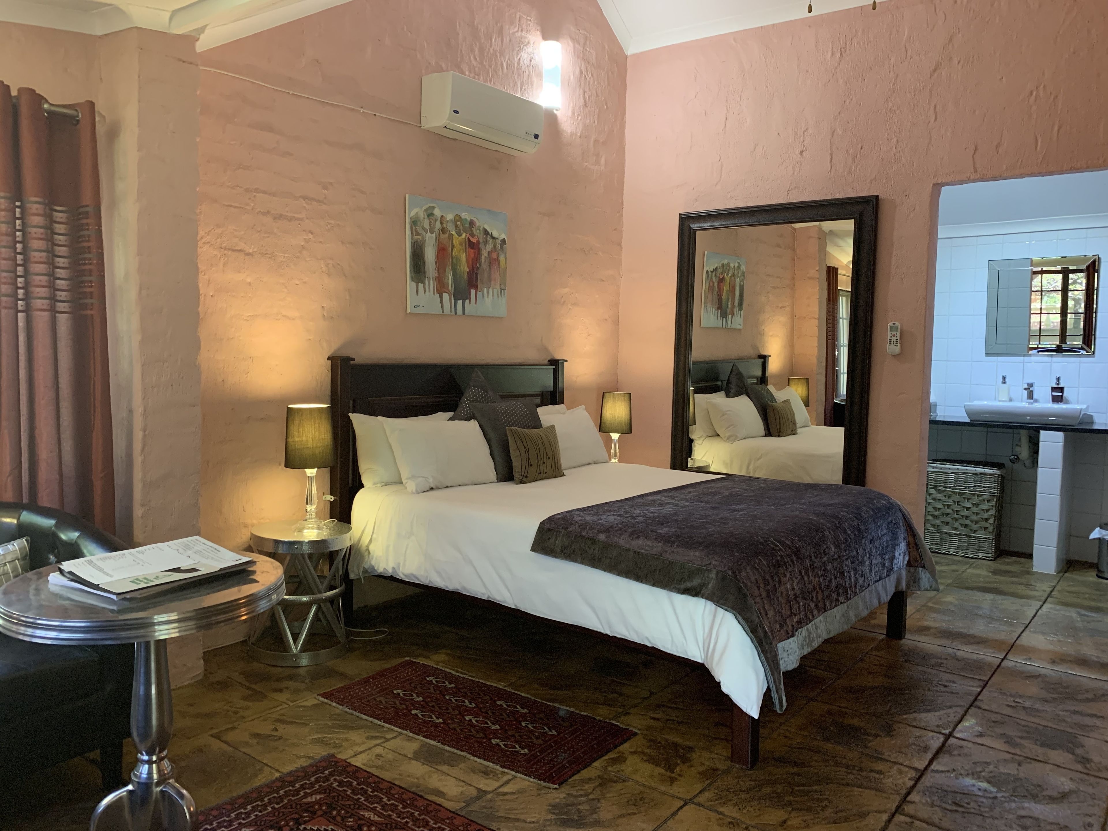 A bedroom with a bed, bedside tables, a mirror, and a bathroom visible through an open door.