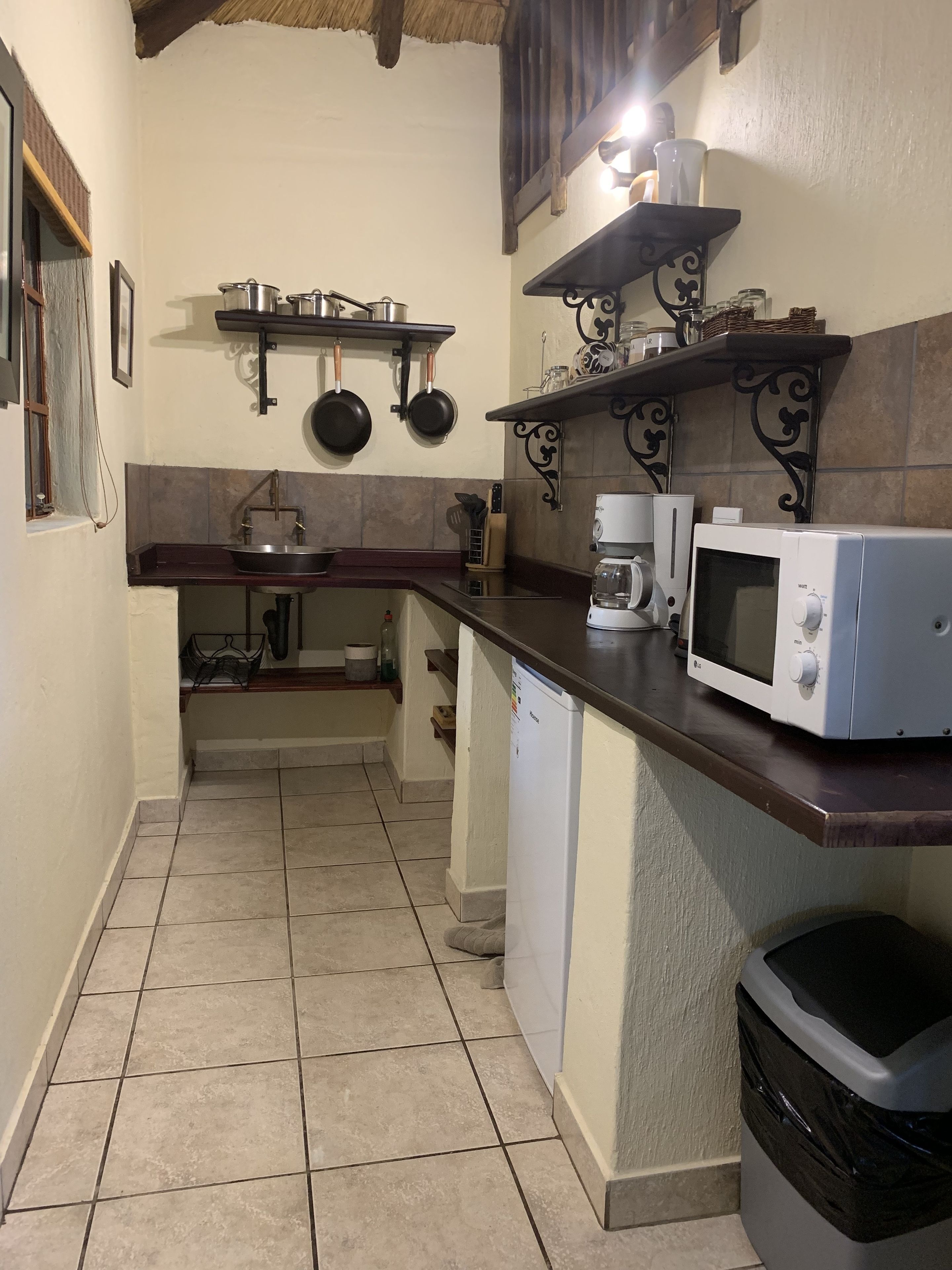 A compact kitchen with a sink, stove, microwave, and shelves with pots and pans.