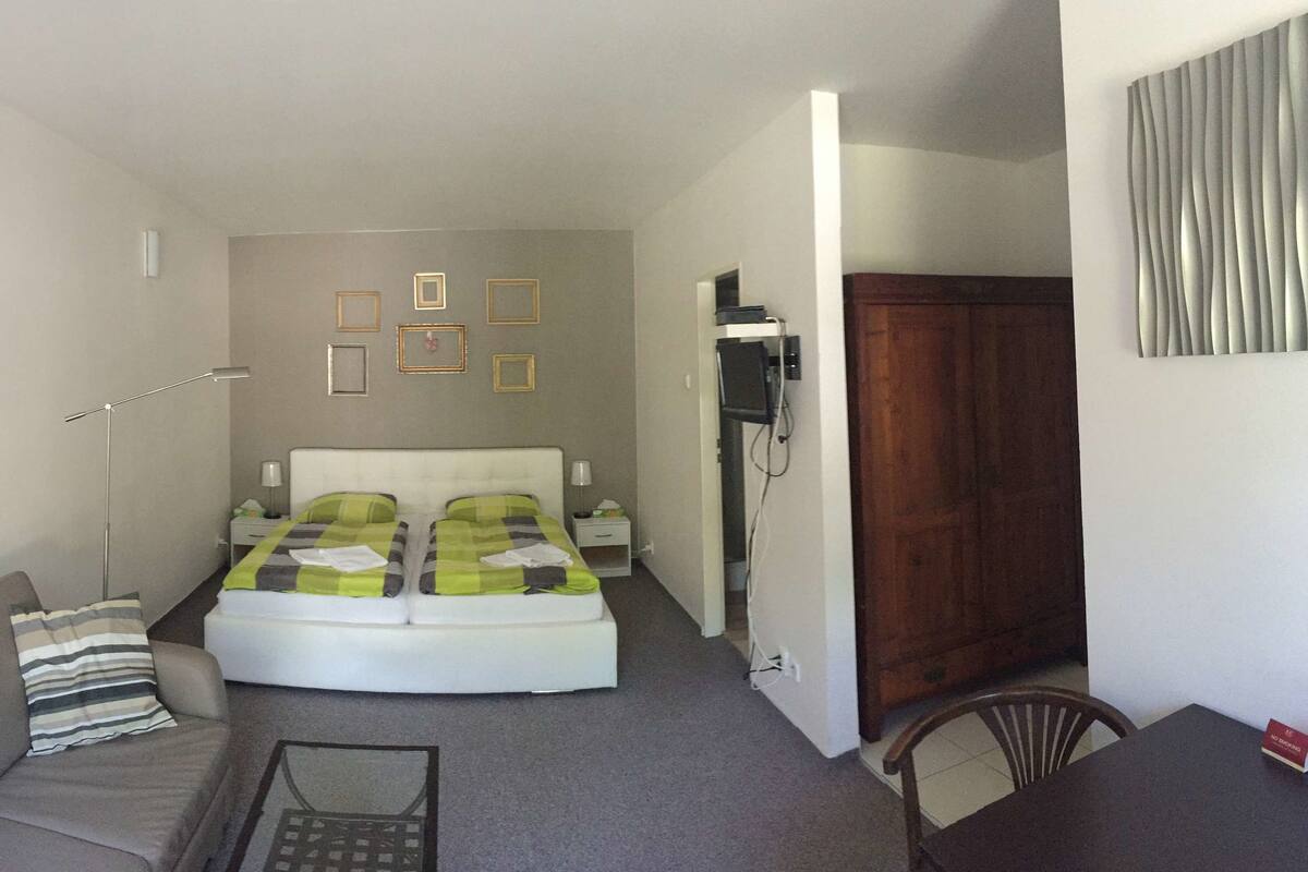 A compact hotel room with a bed, a sofa, a small table, and a desk.