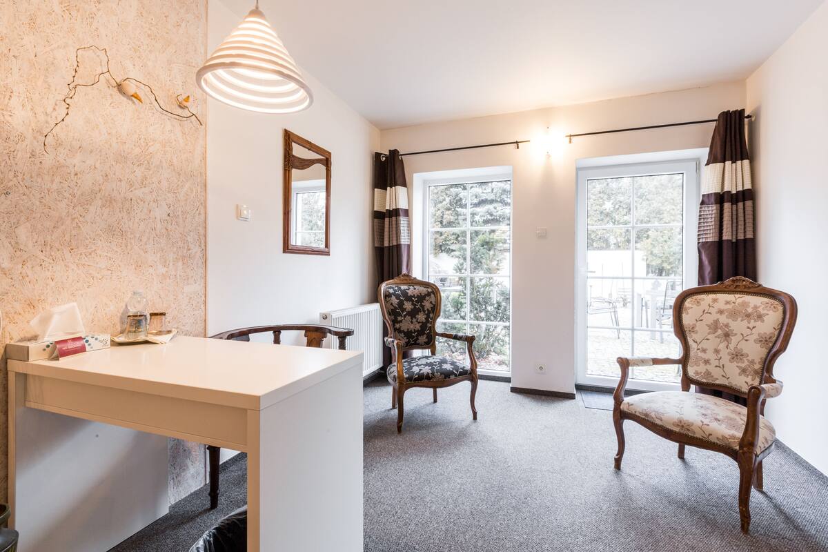 A room with a wooden table, two chairs, a mirror, and a window with curtains.