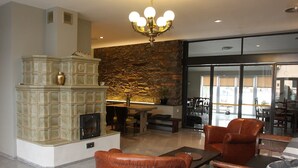 A spacious lobby with a stone wall, a fireplace, leather chairs, and a chandelier. - Alt Pension (Prague)