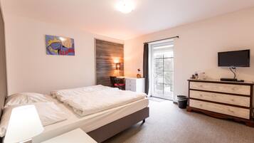 A bedroom with a bed, a desk, a chair, a dresser, a TV, and a window.