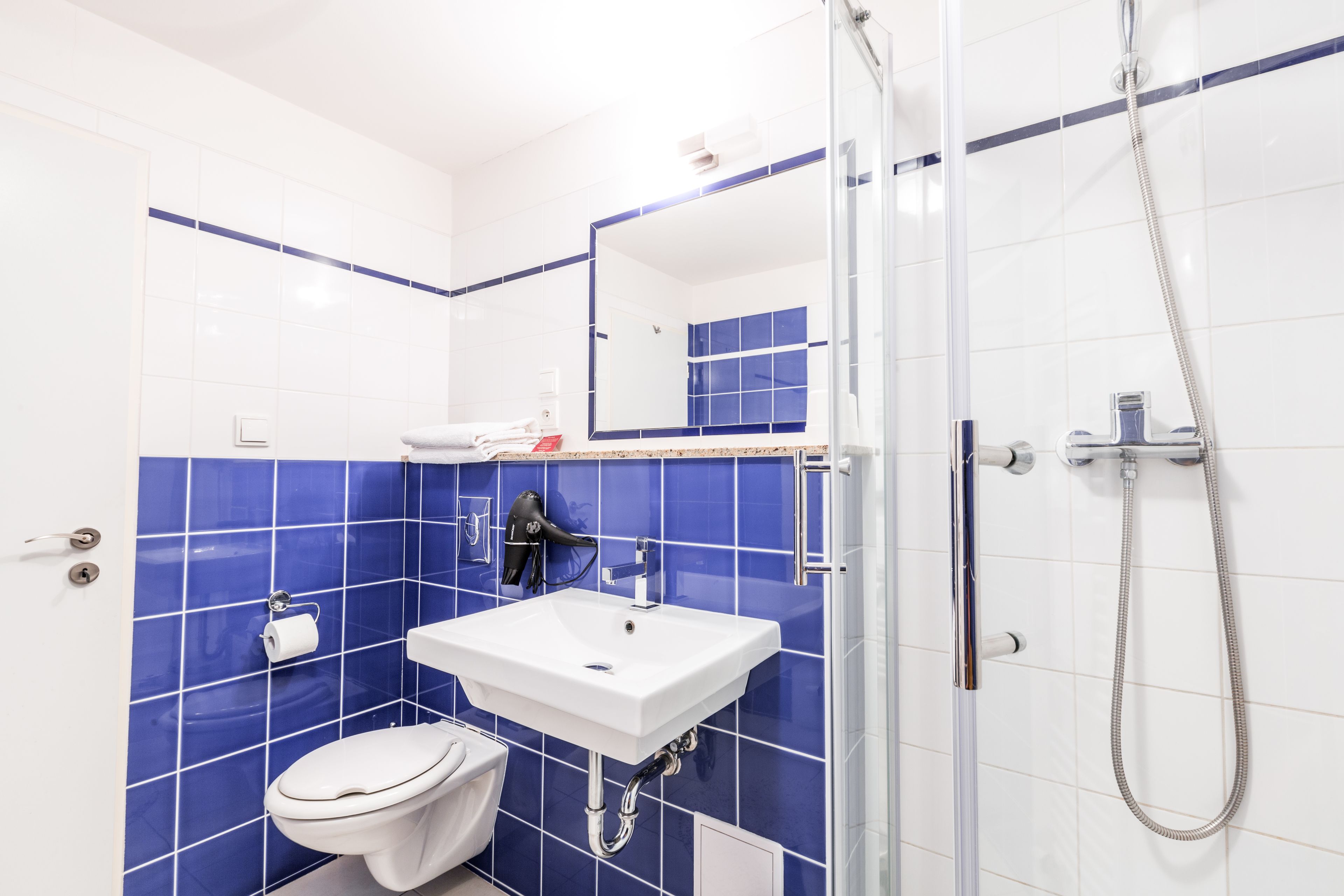 A bathroom with a white sink, blue-tiled walls, a white toilet, and a glass-enclosed shower area.
