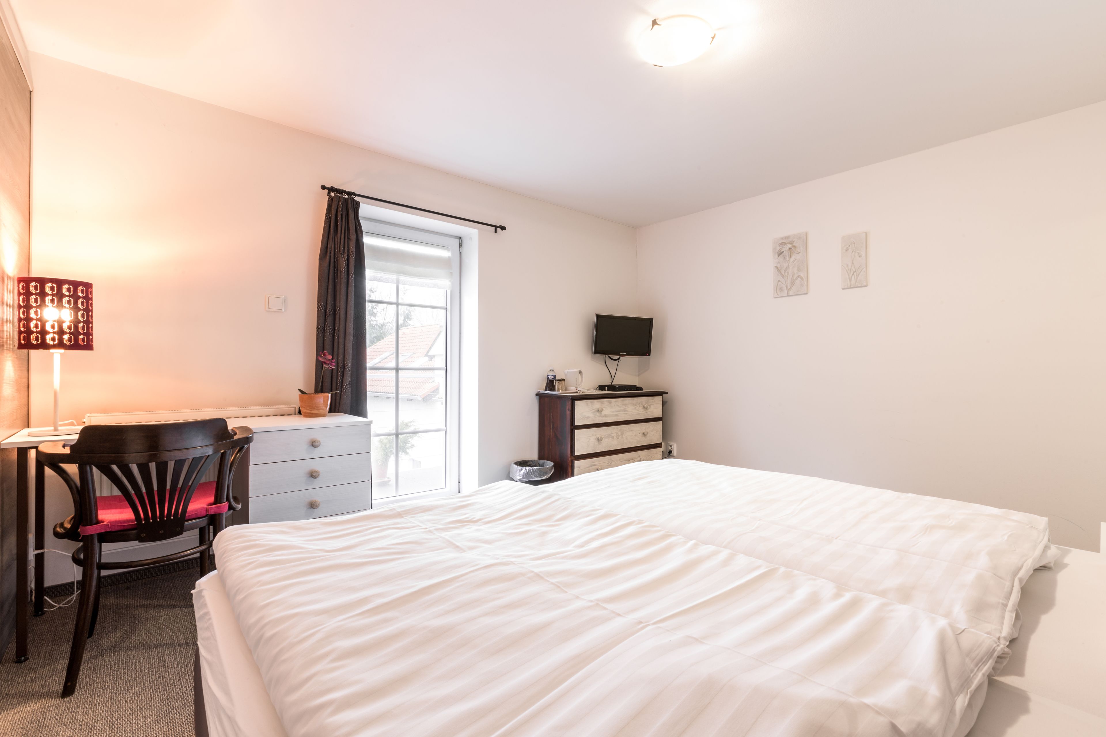 A bedroom with a bed, a desk, a chair, a dresser, and a television.