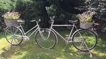 Una bicicleta estática con cestas en las ruedas delantera y trasera, estacionada sobre césped.