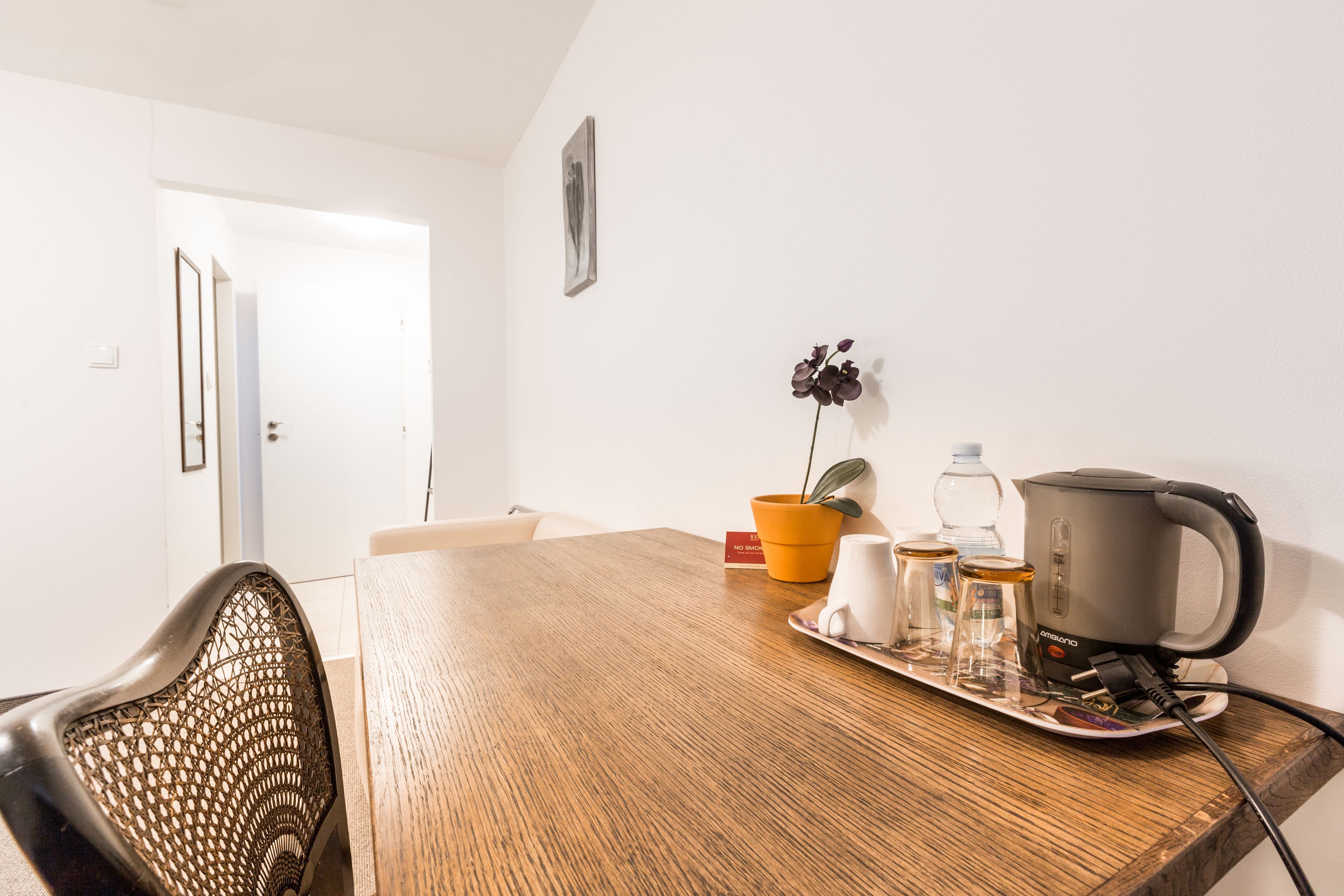 Une table de salle à manger en bois sur laquelle se trouve un plateau contenant une bouilloire, une plante en pot et une bouteille d’eau.