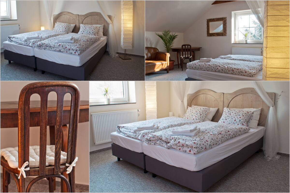 A bedroom with a double bed, a wooden chair, a table, and a potted plant.