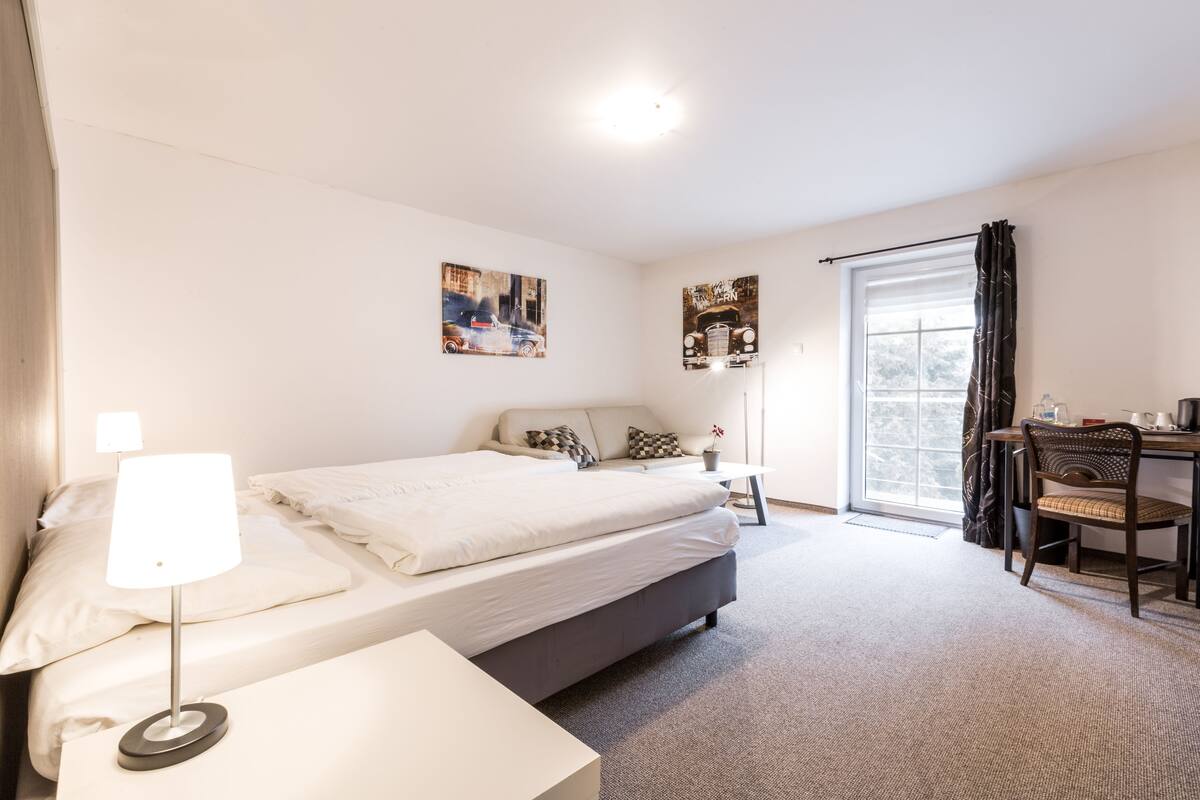 A modern hotel room with a bed, bedside lamp, a desk with a chair, and two wall-mounted artworks.