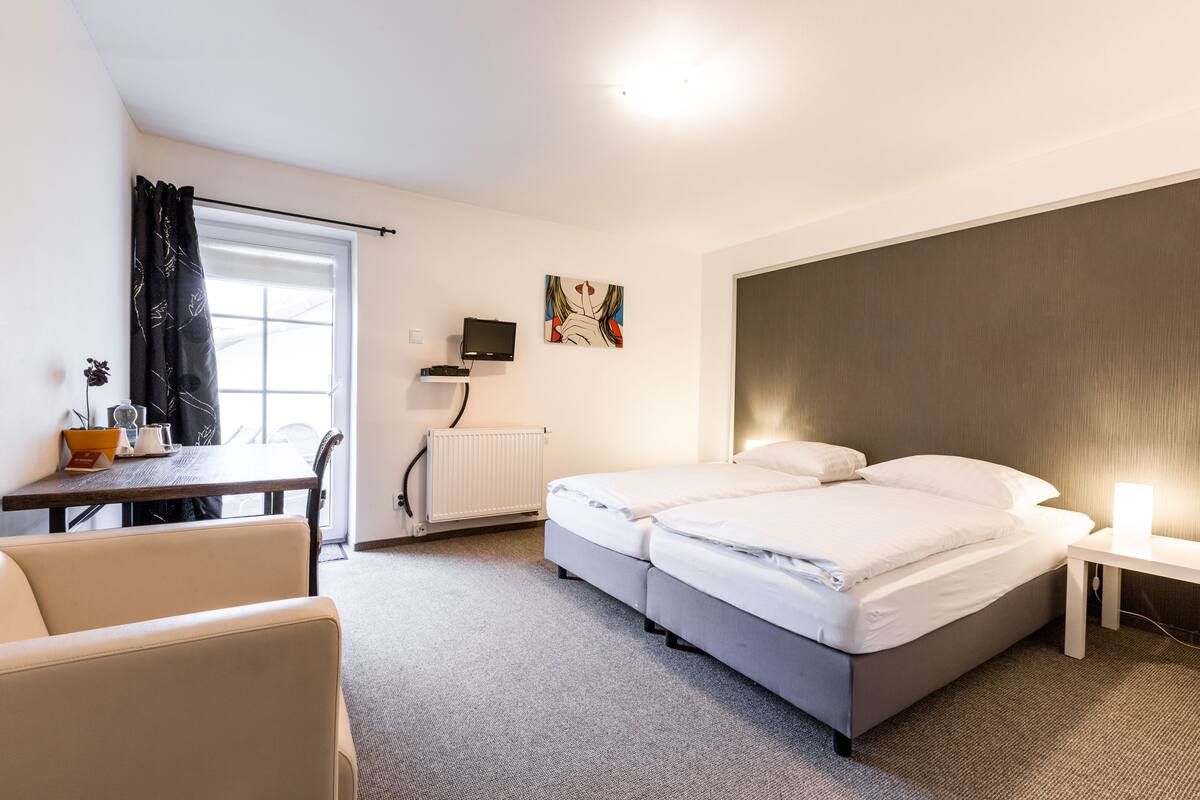 A hotel room with a bed, a desk, a chair, a TV, and a painting on the wall.
