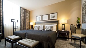 Et hotelværelse med en stor seng, to sengeborde, en stol og et lille bord.