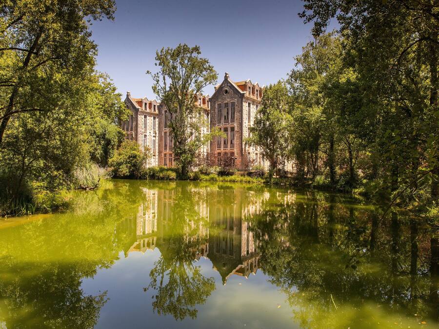 Un bâtiment historique, avec un grand étang devant, entouré d’arbres.