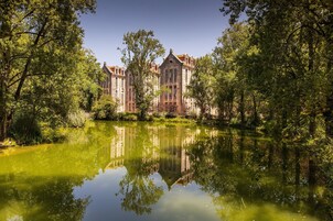 A historic building with a large pond in front, surrounded by trees.