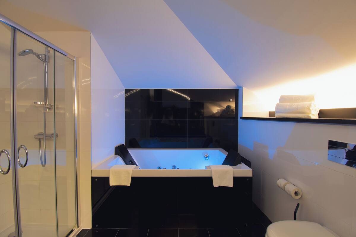 A modern bathroom with a glass-enclosed shower, a freestanding bathtub, and a toilet with a towel rack.