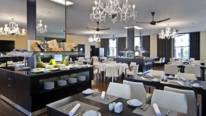 Et moderne hotelspisested med flere borde, lysekroner og et buffetbord.