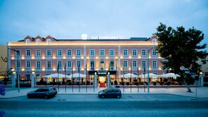 Et hotel med en række vinduer, en rød indgang og parasoller udenfor.
