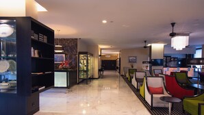 A modern hotel lobby with a marble floor, a black bookshelf, a glass display case, and colorful seating areas. - SANA Silver Coast Hotel (Caldas da Rainha)